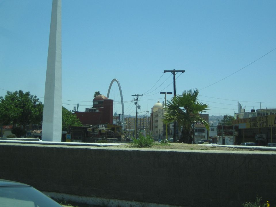 Arched monument and palm tree over a city street seen past a low concrete wall