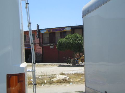 View of a storefront with Spanish signage seen between two parked trailers