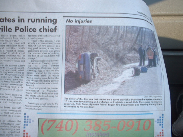 Newspaper clipping with photo of a dark car on its side in a ditch on a rural road, responders nearby