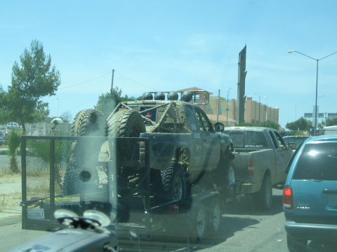 Camouflage off-road truck on a trailer towed by a pickup in traffic