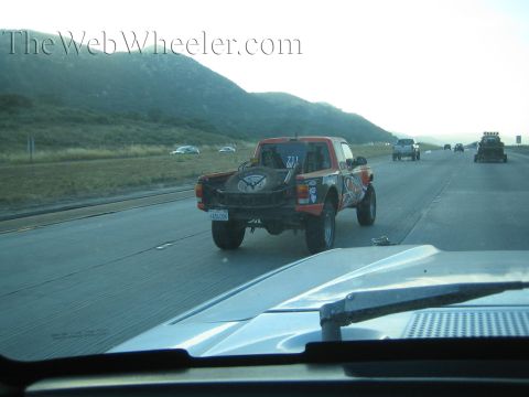 Orange and black off-road race truck number 211 on a highway near hills