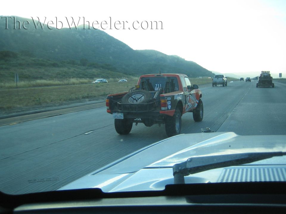 Orange and black off-road race truck number 211 on a highway near hills