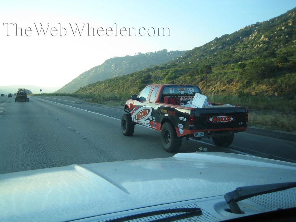 Black and orange off-road race truck driving a highway through hills