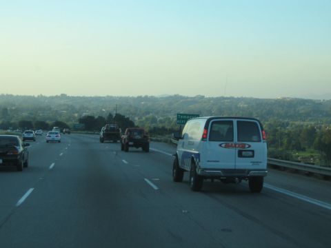 White cargo van and off-road trucks on a highway near a Temecula sign