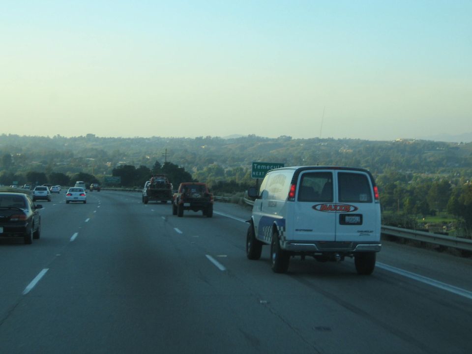 White cargo van and off-road trucks on a highway near a Temecula sign