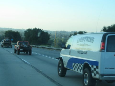 White 'Lightning Industries' van beside a red off-road truck on a highway