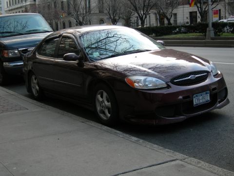 1992 Ford Taurus - This sedan, likely from the early 2000s, is parked curbside on a street with buildings and trees in the background.