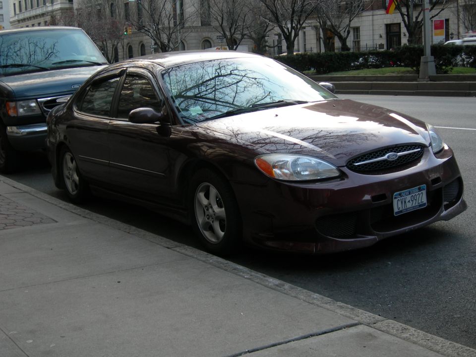 Dark red sedan parked on a city street next to a dark SUV. The sedan has a New York license plate that reads CYK-9922