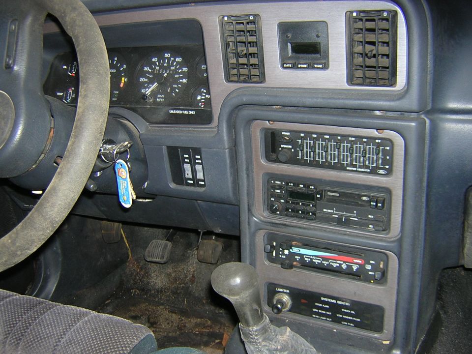1987 Ford Thunderbird interior with a dirty steering wheel, dashboard, and center console with radio and climate controls