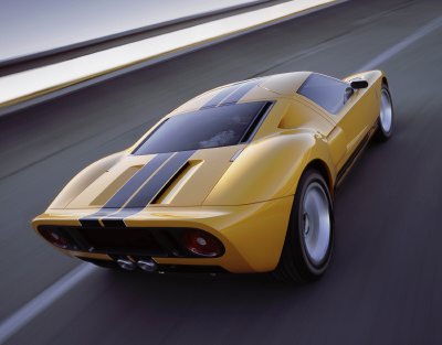 2003 Ford GT - A yellow sports car with black racing stripes is captured in motion on a road.