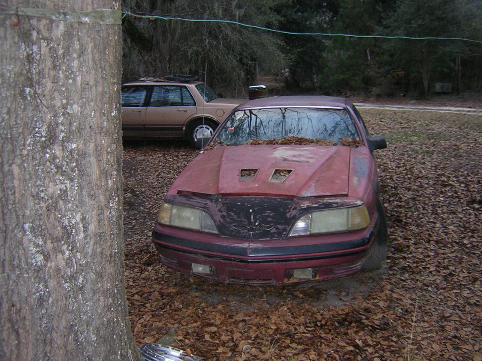 red coupe with hood scoops parked outside, another car behind it