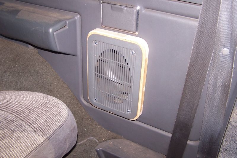 Aftermarket speaker adapter mounted in a car's door panel, next to a seatbelt