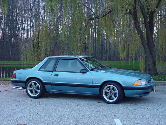 Blue coupe with aftermarket wheels, side view. Appears to be a 1990 Ford Mustang