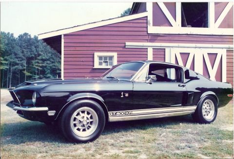 1968 Shelby GT500 - A black 1968 Shelby GT500 is shown in a three-quarter front view, parked on grass before a red barn.