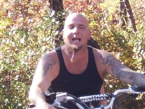 1987 Suzuki Samurai - Man with tattoos and a goatee riding an ATV through a wooded area.