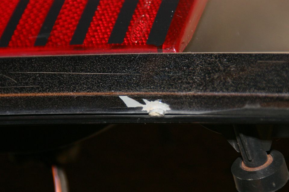 Close-up of black trim below a red tail light with black stripes. There's a chip in the trim