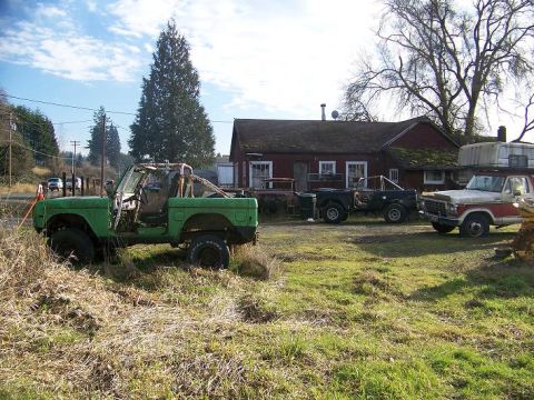 1968 Ford Bronco - Multiple vehicles are parked in a grassy yard in front of a red building.