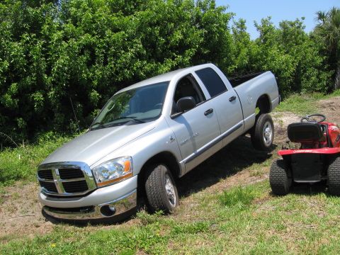 1974 Ford F-100 - Silver Dodge Ram pickup truck is parked on an incline next to a red riding mower.