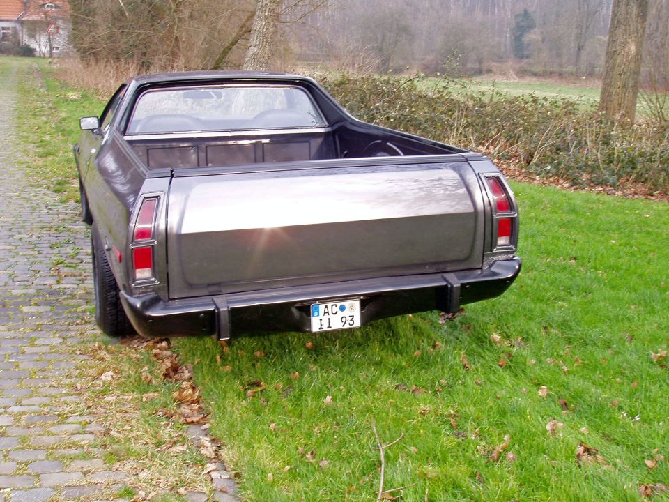 Dark gray 1972 Ford Ranchero rear quarter view, parked on grass next to a cobblestone path