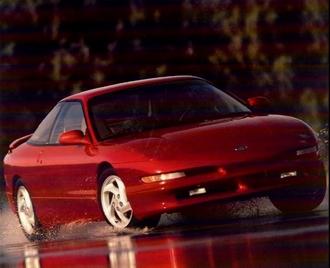 1988 Mazda MX-6 - A red 1989 Ford Probe is captured in motion, splashing through water on a wet road.