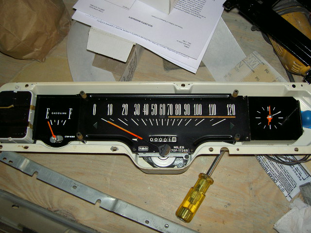 Car instrument cluster with speedometer, fuel gauge, and clock. A screwdriver is inserted