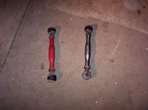 1987 Jeep Cherokee - Two suspension control arms, one red and one silver, are shown on a concrete surface.