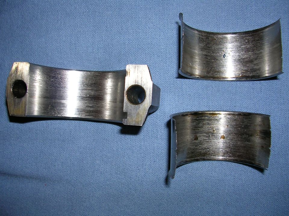 Three worn engine bearing shells with visible scoring and oil residue on a blue cloth background