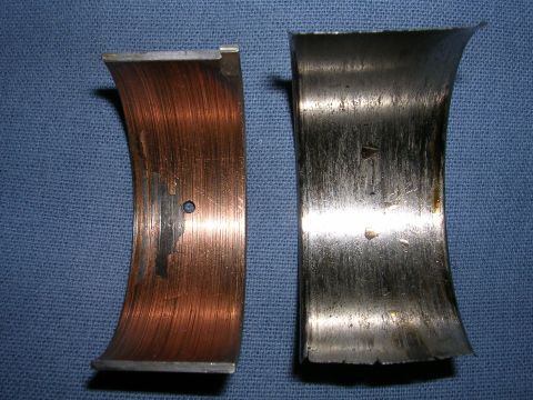 1996 Ford Probe - Comparison of a worn copper engine bearing and a worn metal engine bearing, likely showing signs of engine damage.