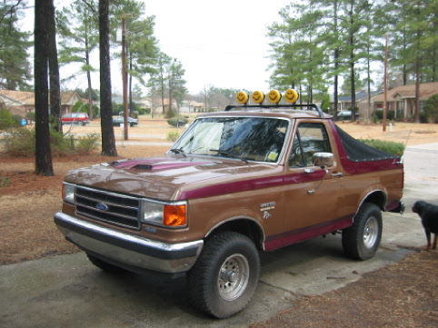 Brown and maroon 1989 Ford Bronco with a soft top and roof lights