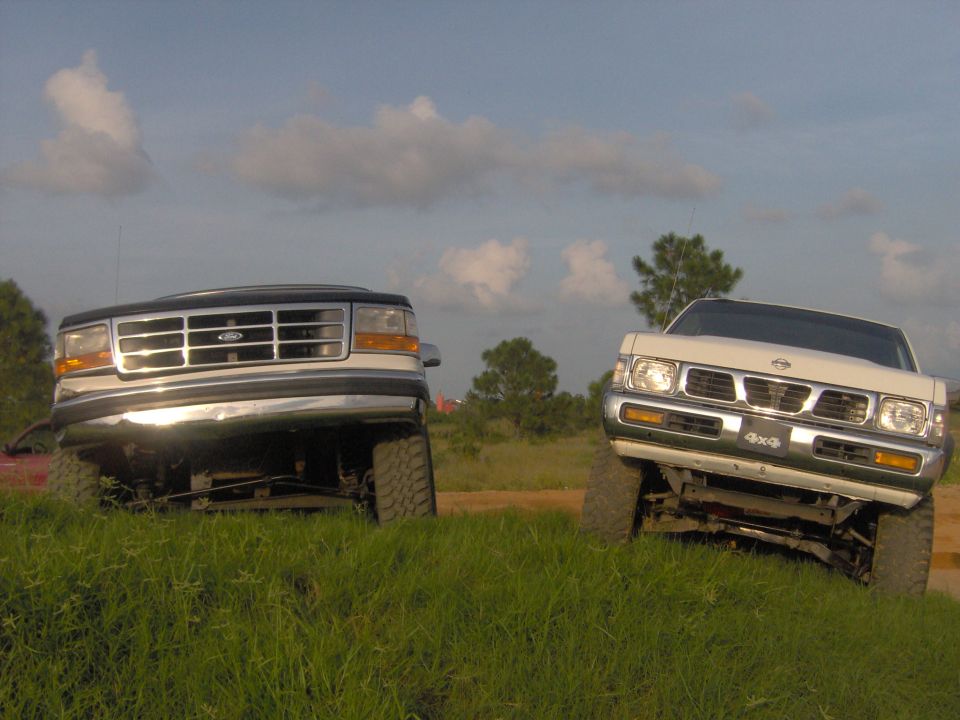 Two trucks are parked on a grassy incline, one black and one white, with the front ends facing the camera
