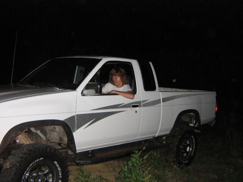 1974 Ford F-100 - A white pickup truck with distinctive grey graphics on its side is shown at night, a lifted suspension and a person inside.