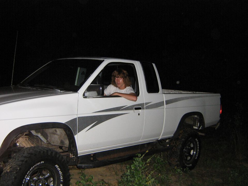 White pickup truck with grey graphics, lifted suspension, and a person in the driver's seat