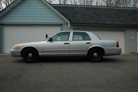 2003 Ford Crown Victoria - Side view of a silver 2003 Ford Crown Victoria sedan, equipped with police lights, parked in front of a residential garage.