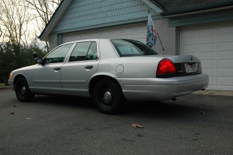 2003 Ford Crown Victoria - Rear view of a silver 2003 Ford Crown Victoria police car parked in front of a garage.