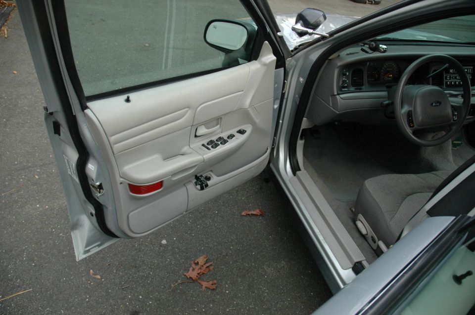 Open driver's door of silver Ford sedan showing gray door panel, cloth seat and dash