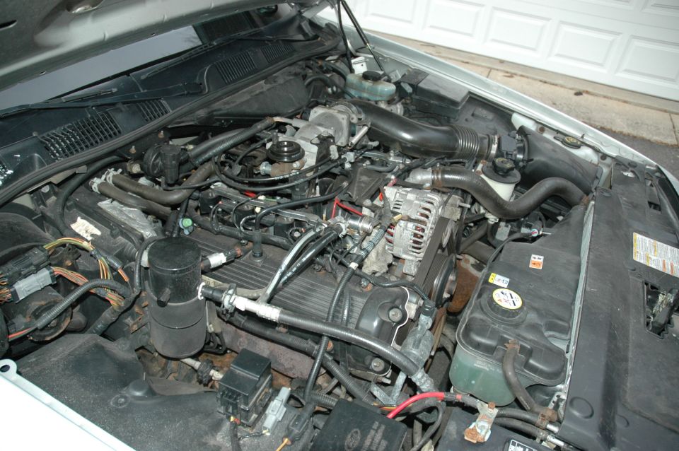 Overhead view of a V8 engine bay with intake duct, alternator and coolant reservoir
