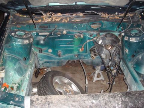 1993 Ford Taurus - The engine bay of a green vehicle is shown, with the engine removed and a spare tire visible below.