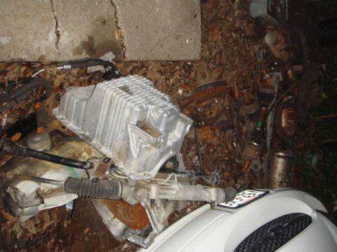 1993 Ford Taurus - Various engine and steering components are piled on the ground next to a concrete wall.