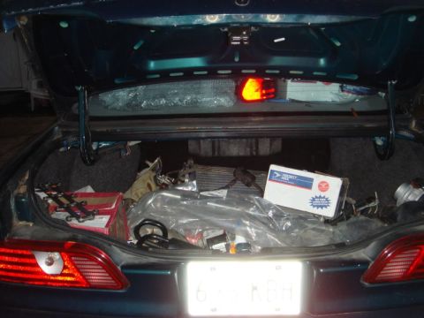 1993 Ford Taurus - The open trunk of a car is packed with assorted items, including a box of mail and plastic-wrapped components.