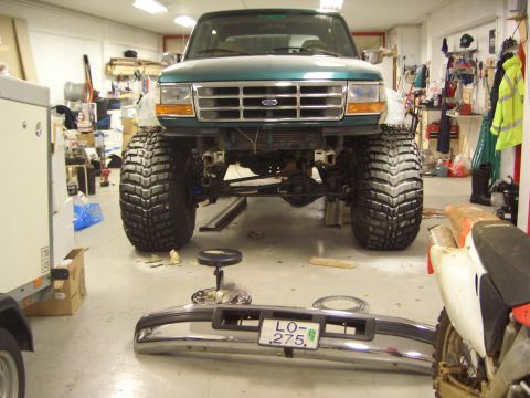 1996 Ford Bronco - A green Ford Bronco is parked in a garage, undergoing modifications with a detached bumper in the foreground.