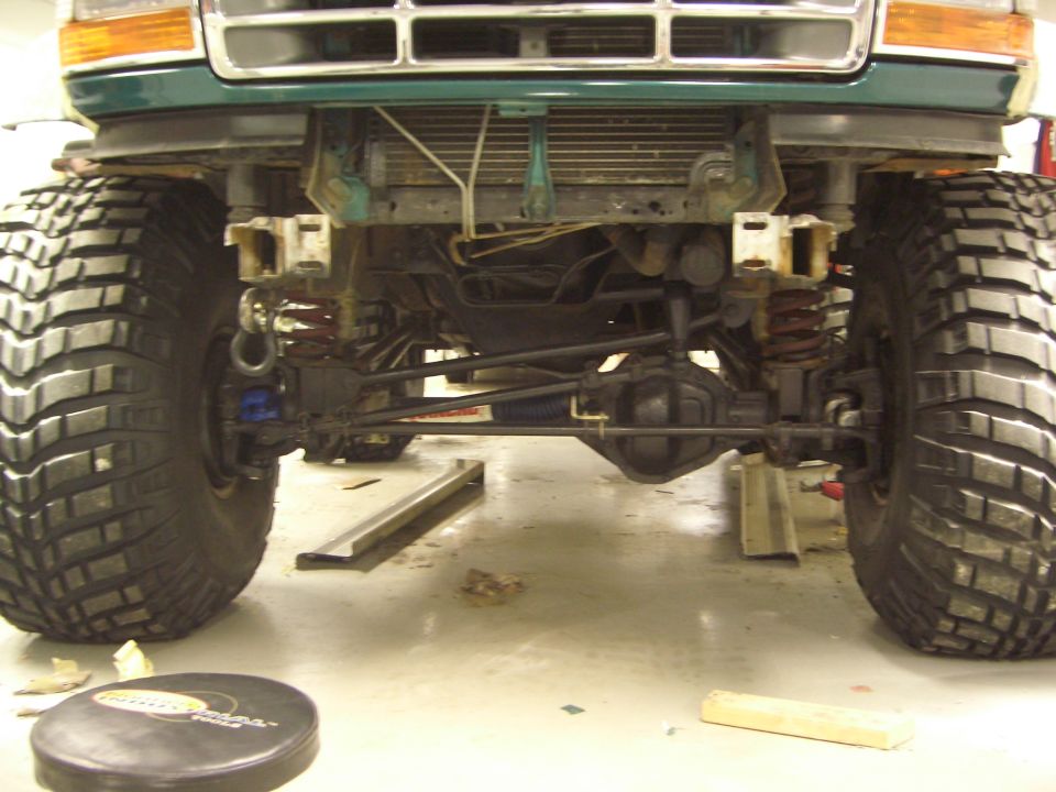 Underside front axle and suspension of a lifted green Ford Bronco on oversized mud tires
