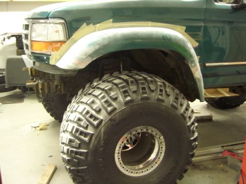 1996 Ford Bronco - A close-up view of a green Ford Bronco's front fender and massive off-road tire, showing modifications in progress.