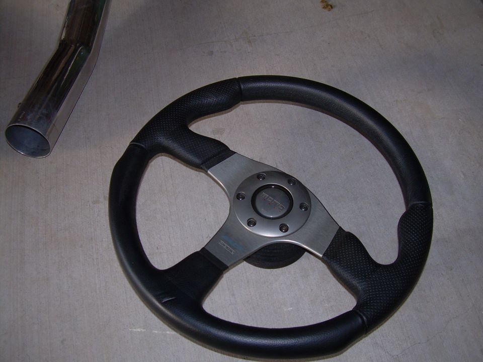 Momo steering wheel with textured grips and metal spokes, next to a chrome exhaust pipe