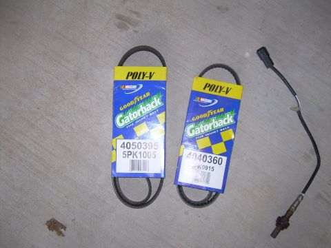 1996 Ford Probe - Two Goodyear Gatorback belts and an oxygen sensor are laid out on a concrete surface.