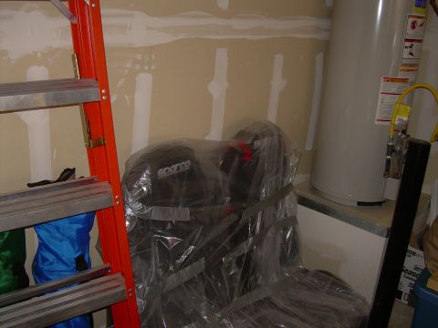 1996 Ford Probe - Two black Sparco car seats are wrapped in plastic and secured with tape, next to a water heater and ladder.
