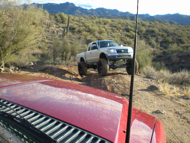 Silver Toyota Tacoma pickup truck lifted with large tires on a dirt road