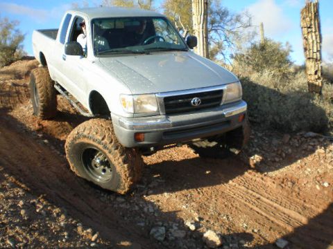 1991 Ford Bronco - Toyota Tacoma pickup truck navigating a dirt trail in a desert environment.