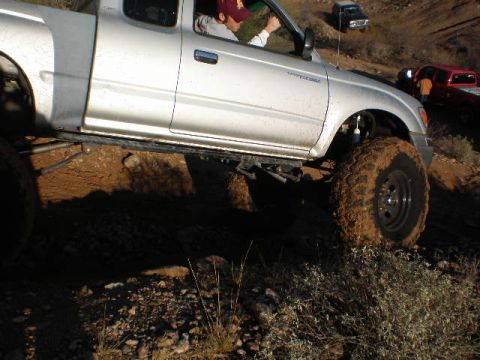 1991 Ford Bronco - A silver pickup truck navigates a rough, muddy terrain with other vehicles in the distance.