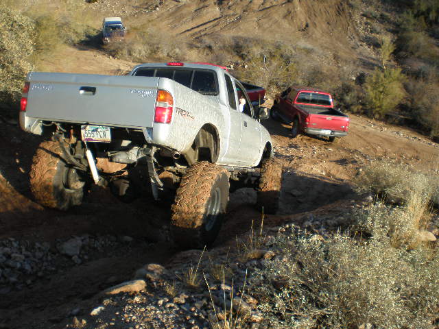 Silver Toyota Tacoma pickup truck with lifted suspension and large tires on a dirt trail
