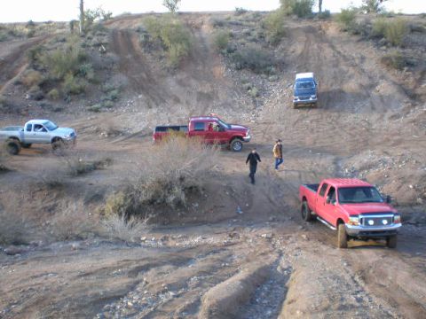 1991 Ford Bronco - Several trucks and SUVs navigate a challenging dirt terrain, with a red Ford F-250 prominent in the foreground.